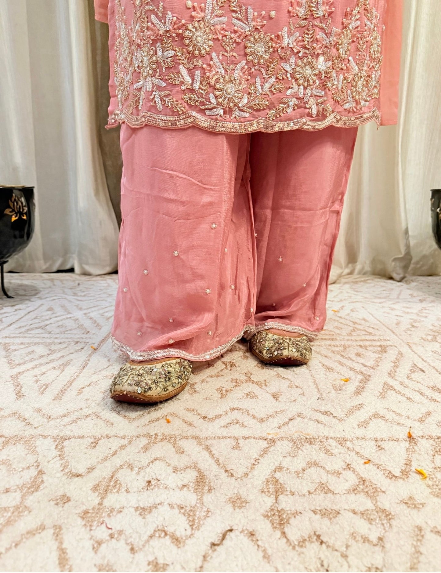 Person wearing a pink traditional outfit with floral embroidery on a patterned carpet. DUSTY_ROSE_EMBROIDERED_CHINON_SUIT