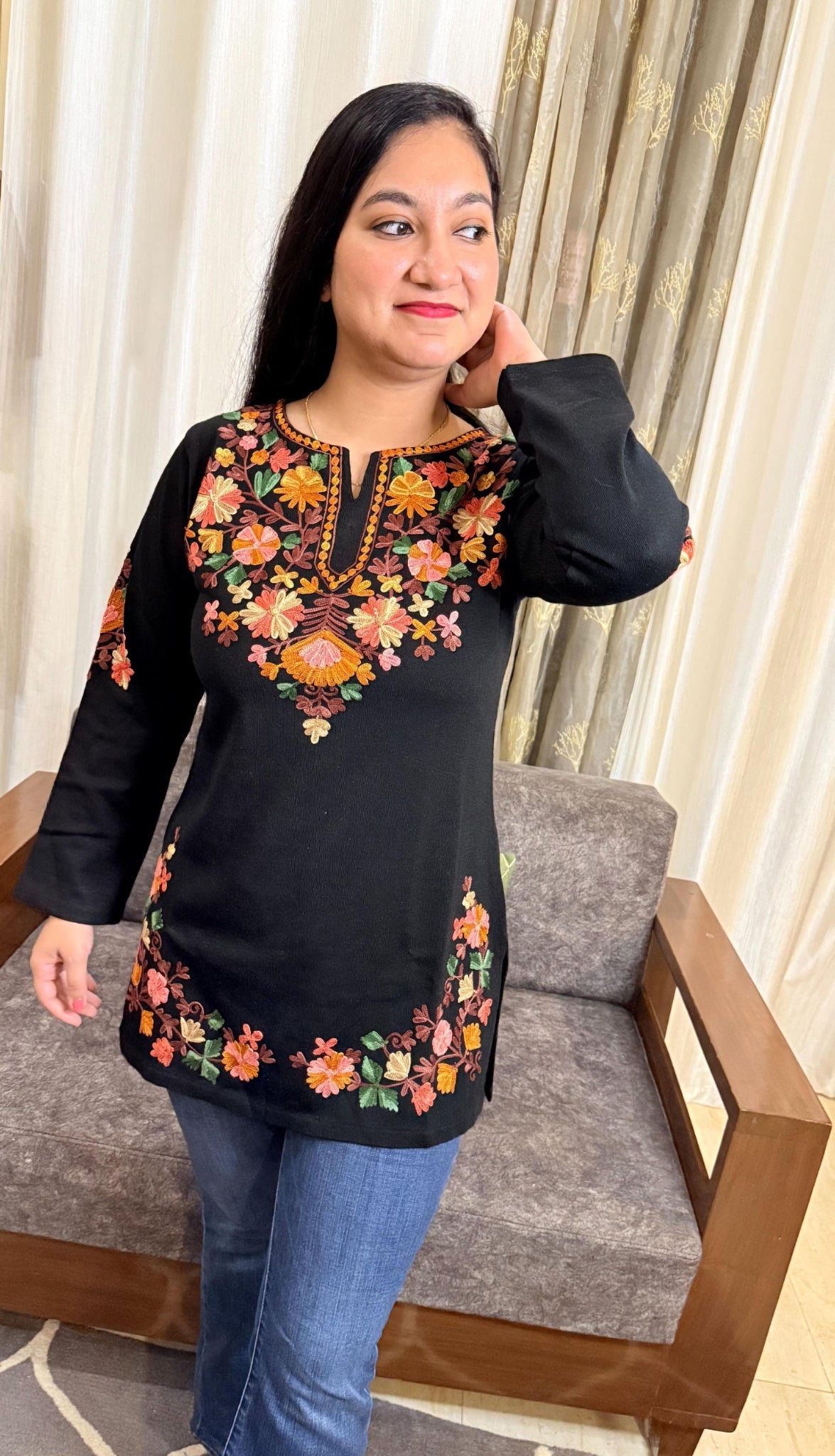 Woman wearing a black embroidered top in a living room setting GulmoharBlackEmbroideredKashmiriWoollenKurti2