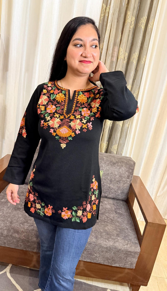 Woman wearing a black embroidered top in a living room setting GulmoharBlackEmbroideredKashmiriWoollenKurti2