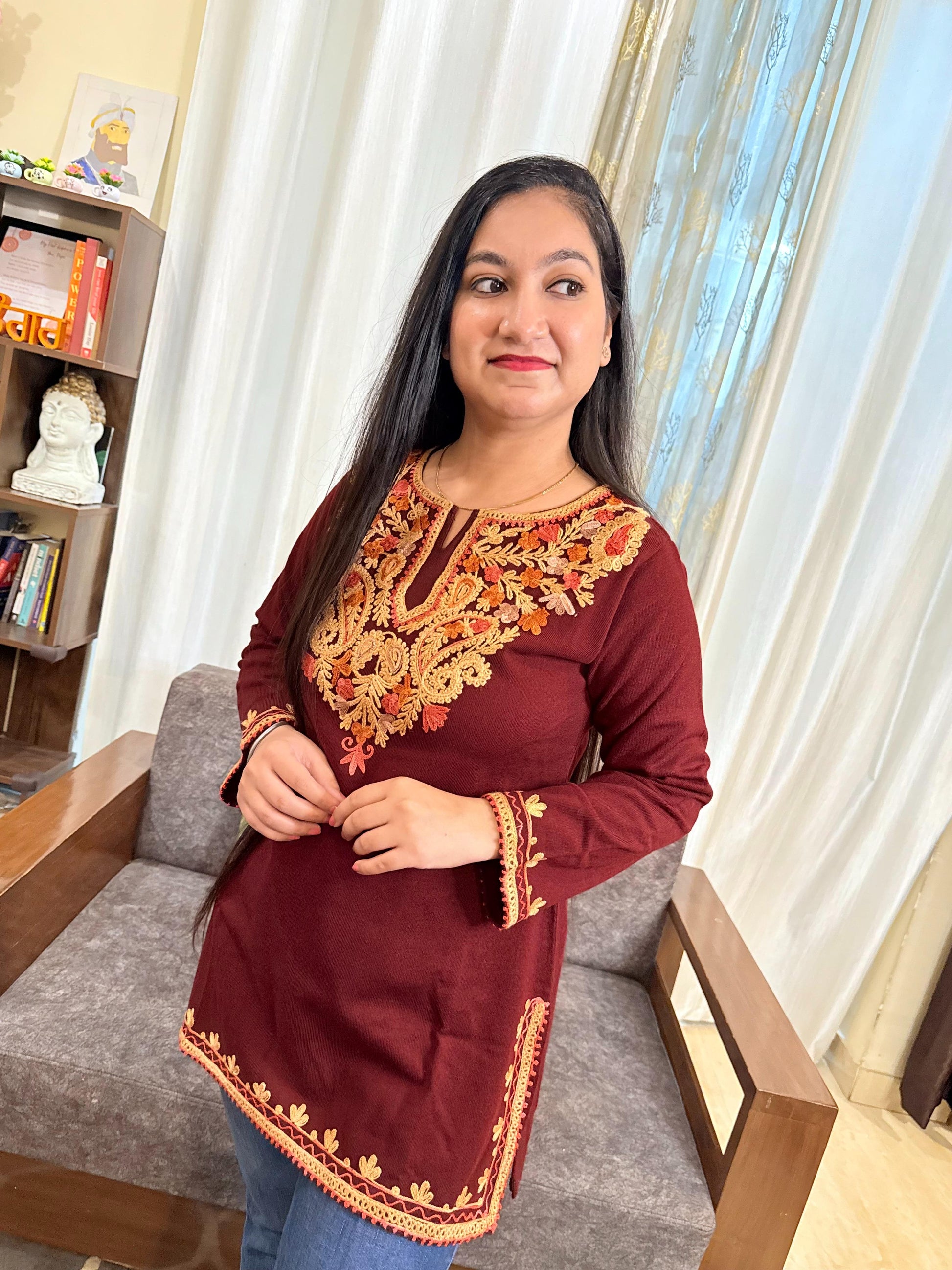 Woman wearing a maroon top with intricate gold embroidery in a home setting.