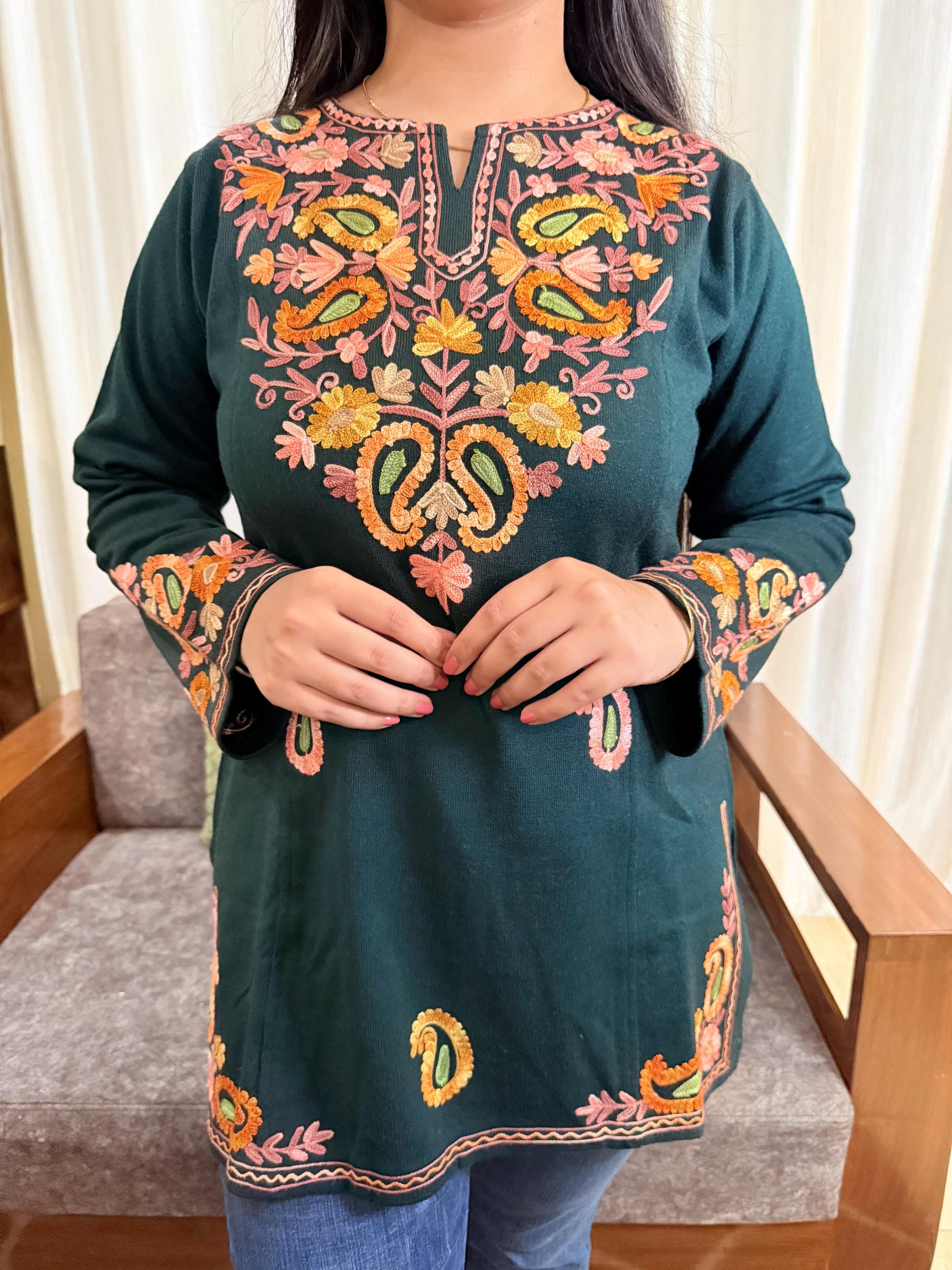 Green embroidered top worn by a person, sitting on a chair with a neutral background GulmoharTealEmbroideredKashmiriWoollenKurti3