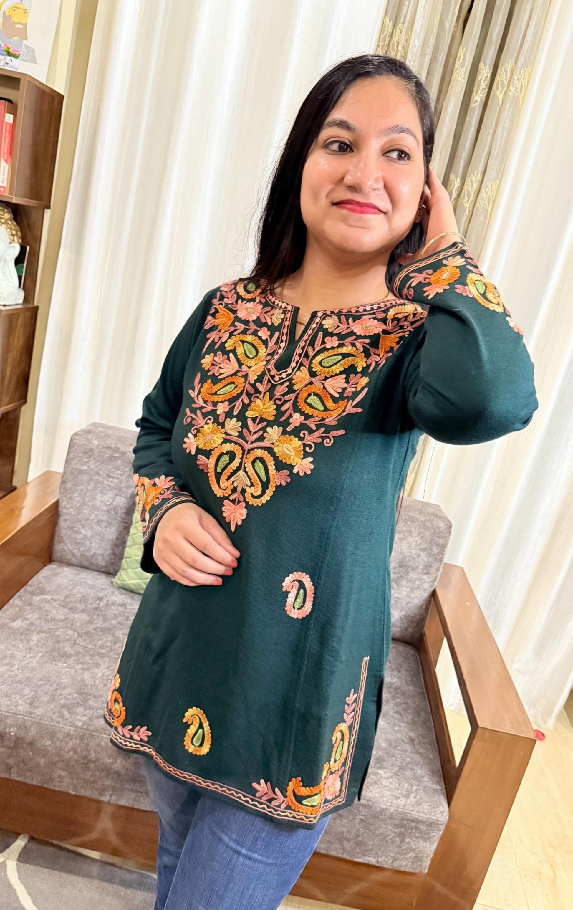 Woman wearing a green embroidered top in a living room setting GulmoharTealEmbroideredKashmiriWoollenKurti3