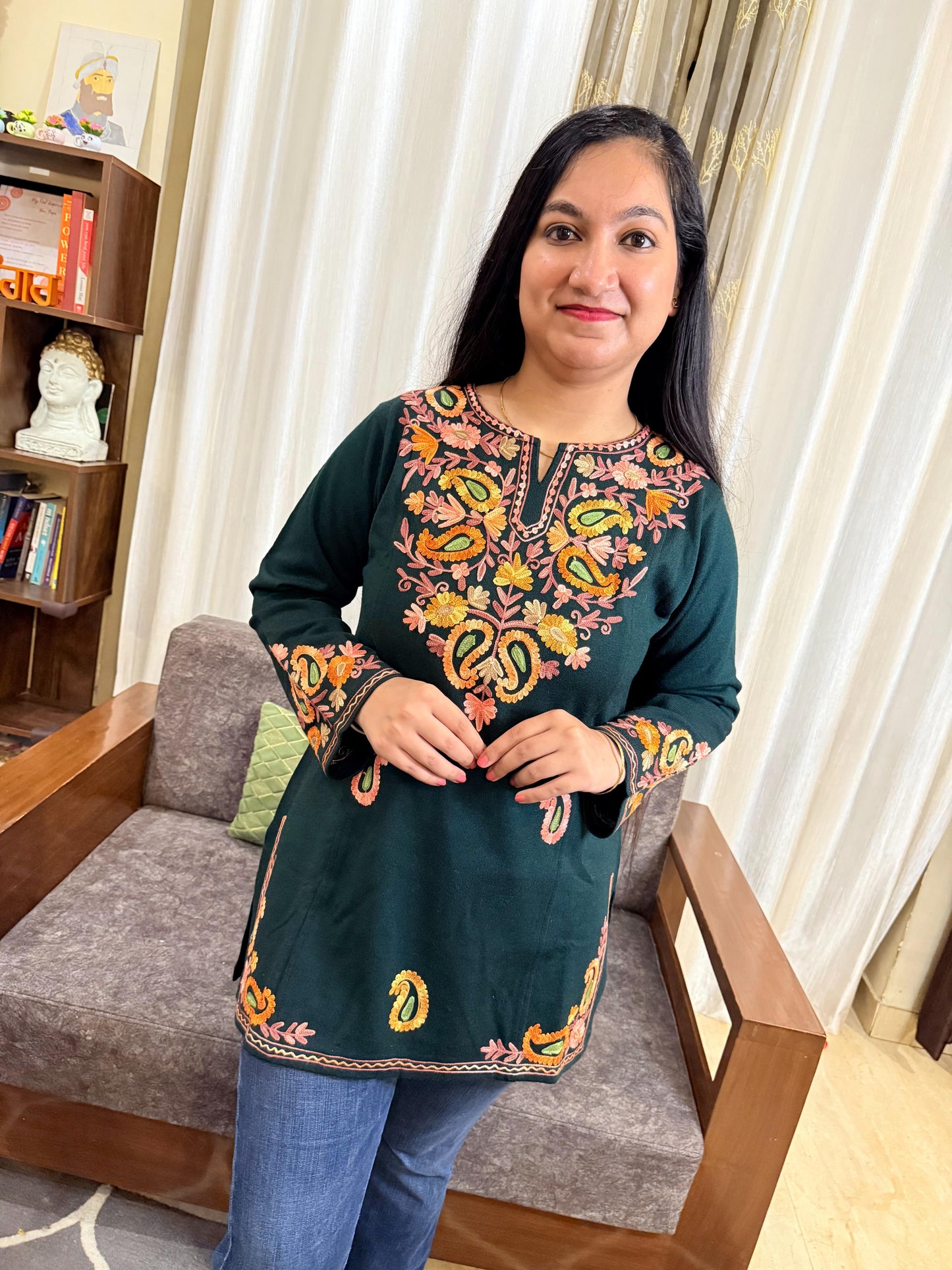 Woman wearing a green embroidered top in a living room setting GulmoharTealEmbroideredKashmiriWoollenKurti3