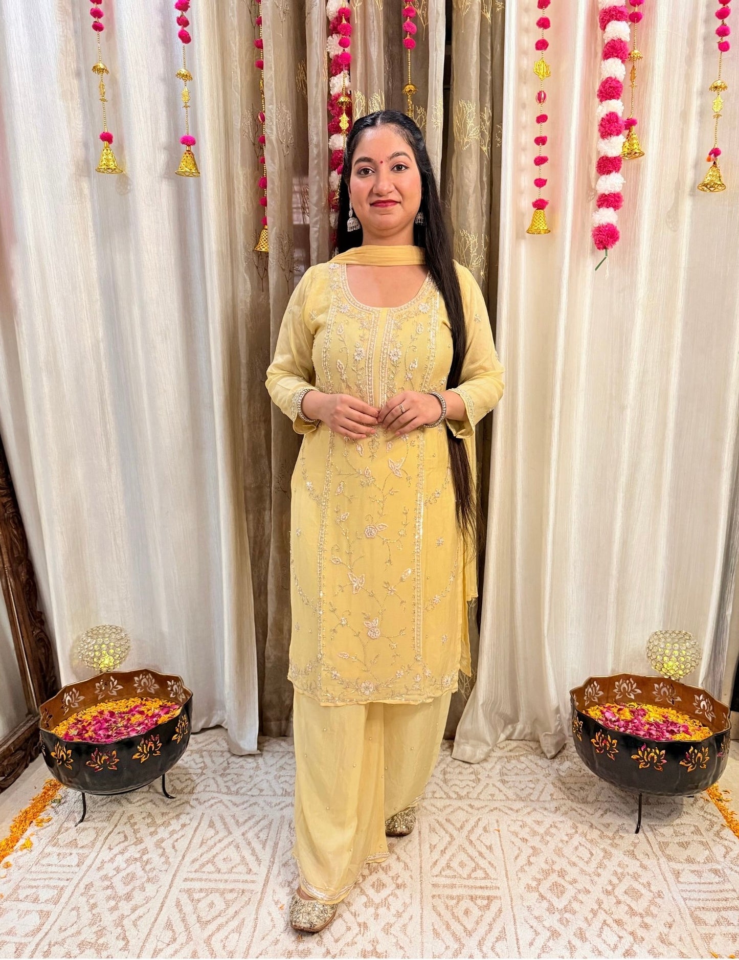 Woman in a yellow traditional outfit standing in a decorated room with white curtains and floral decorations. Lemonlight_Embroidered_Chinon_Suit