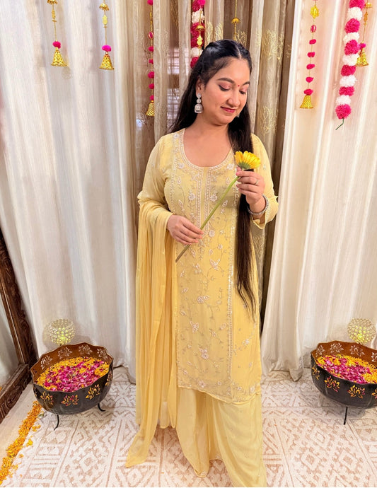 Woman in a yellow traditional outfit holding flowers indoors with decorative elements.Lemonlight_Embroidered_Chinon_Suit