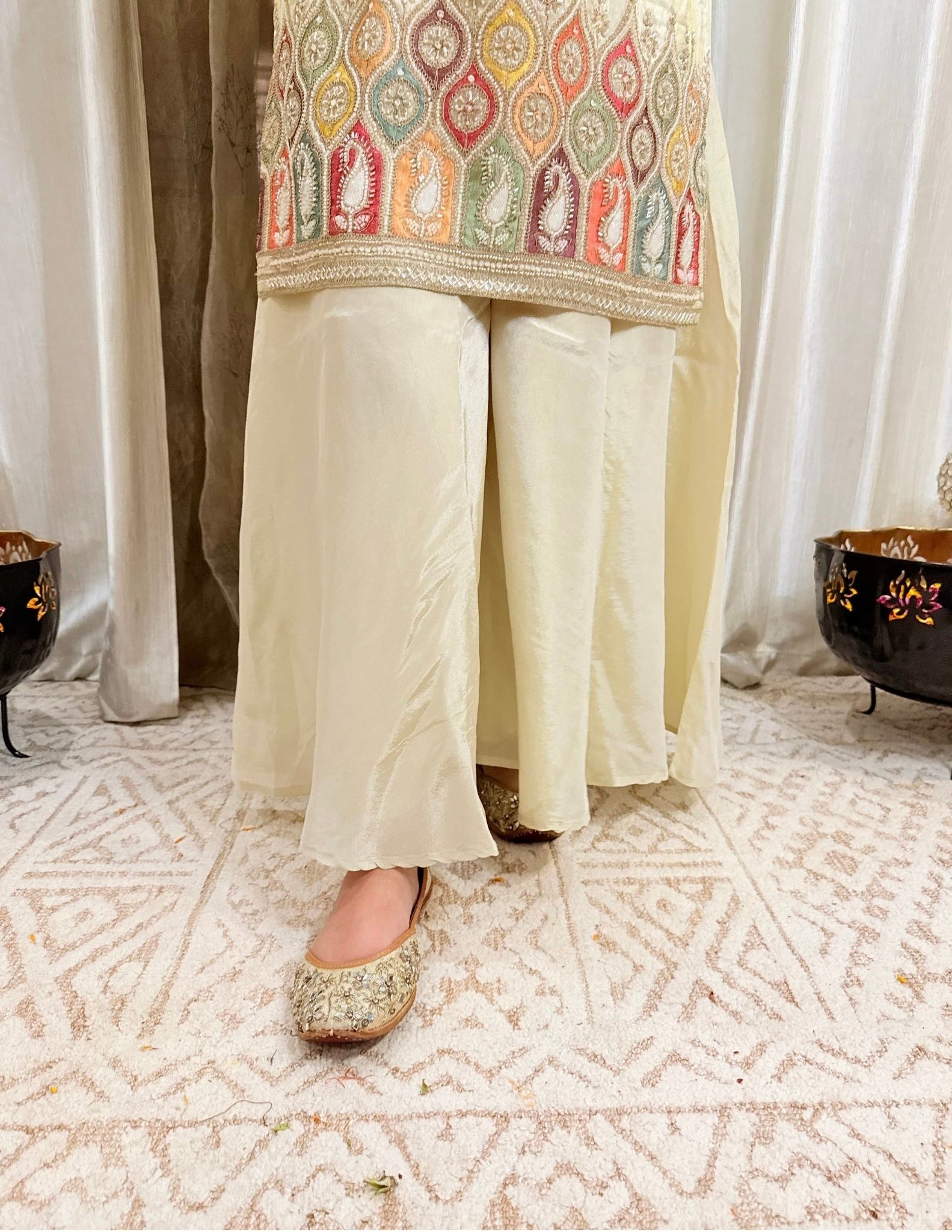 Traditional outfit with embroidered top and light-colored pants on a patterned floor.