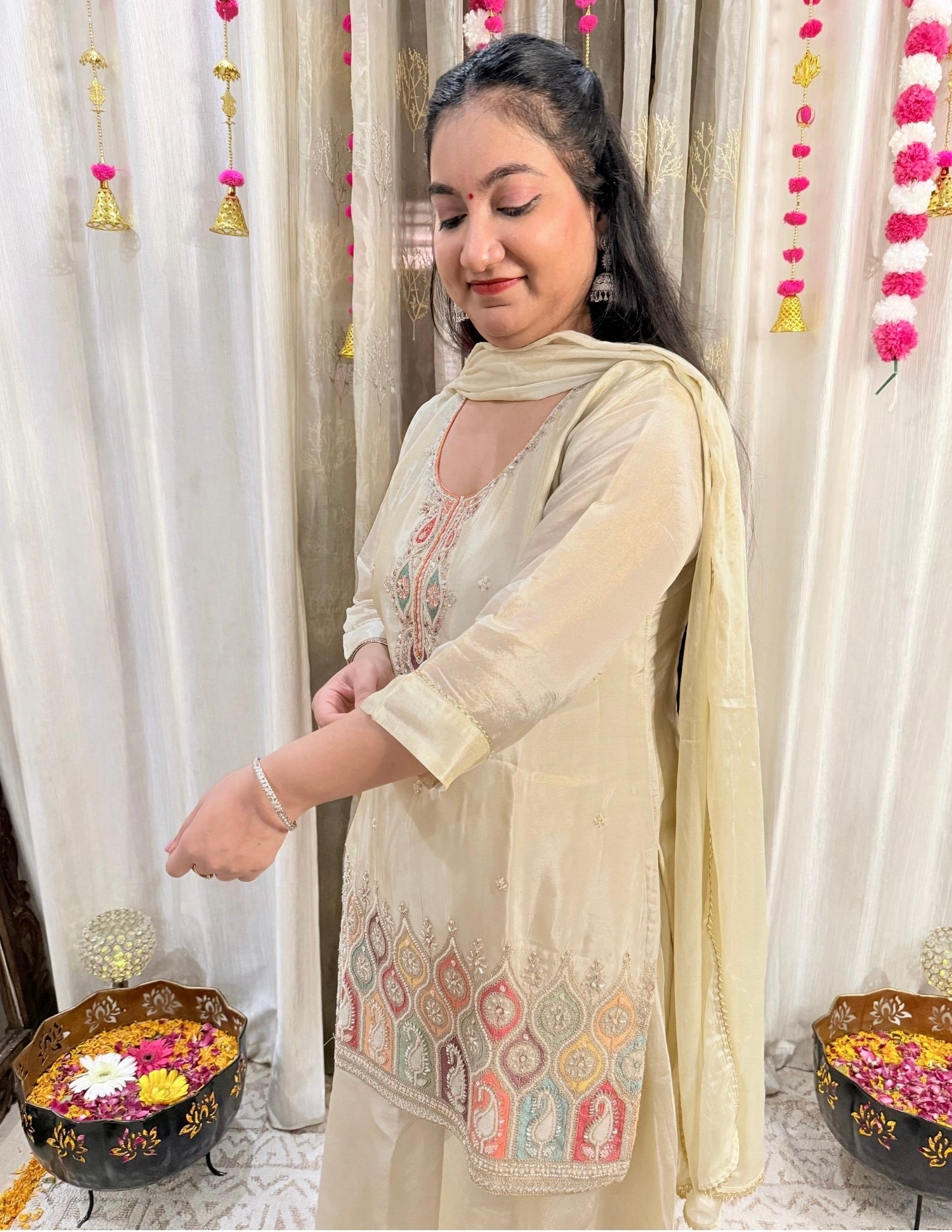Woman in traditional outfit with decorative elements in a festive setting. Noor Ivory Embroidered Flared Palazzo Suit