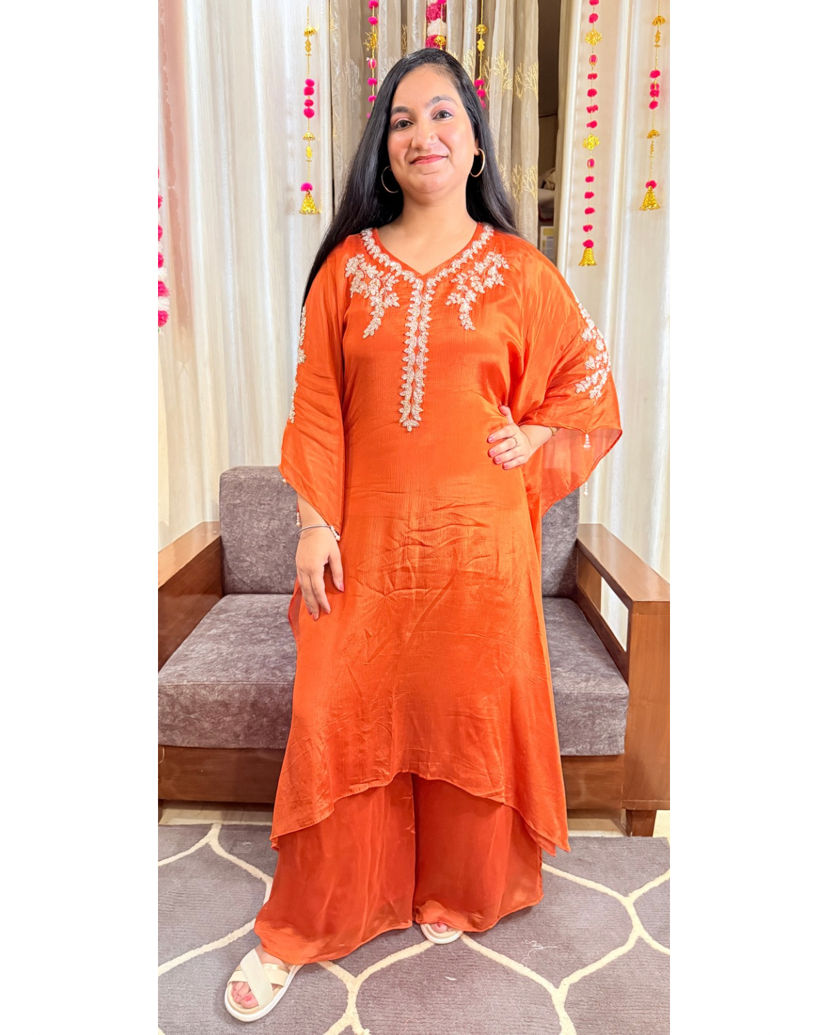 Woman wearing an orange traditional outfit with white embroidery indoors. saffron shine festive kaftan set